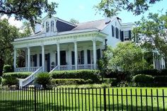 a large white house sitting on top of a lush green field next to a black fence