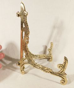 a gold colored metal object that is on a white surface with a hand holding it