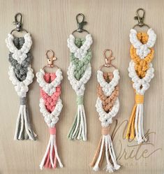 four keychains with different colors and designs hanging on a wooden surface in the shape of hearts