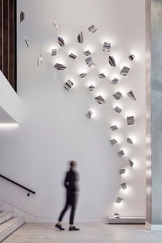 a person standing in front of a white wall with many books on it and some stairs