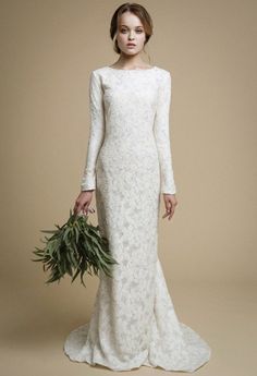 a woman in a white wedding dress holding a green plant and looking at the camera