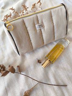 a small white purse sitting on top of a bed next to a bottle of perfume