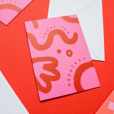 two pink and white envelopes sitting next to each other on top of red paper