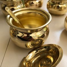 several shiny metal bowls and spoons on a white counter top with gold colored dishes