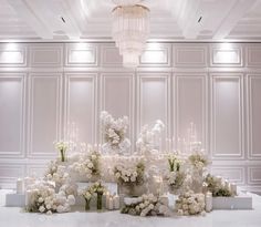 a room with white flowers and candles on the floor in front of a chandelier