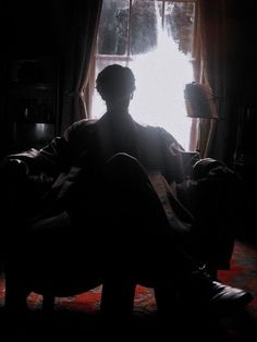 a man sitting on a couch in front of a window with the sun shining through it