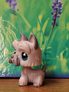 a little pony toy sitting on top of a wooden table next to a purple flower