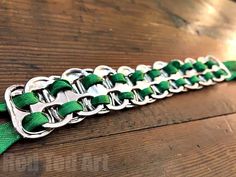 a close up of a green and silver bracelet on a wooden table with metal clasps