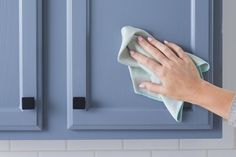 a person wiping up some blue cabinets with a rag