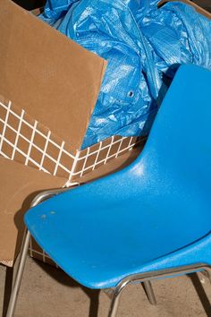 a blue plastic chair sitting next to a cardboard box and some other boxes on the floor