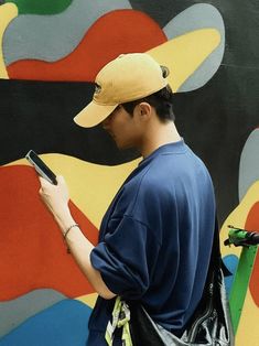 a man standing in front of a colorful wall holding a cell phone and looking at it