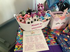 a table topped with lots of stuffed animals next to a sign that says adopt a unicorn