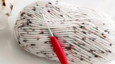 a ball of white yarn with a red crochet hook in the middle next to it