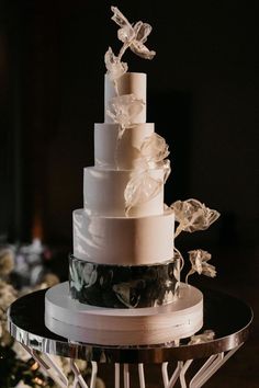 a three tiered wedding cake with white flowers on the top and black bottom, sitting on a glass stand