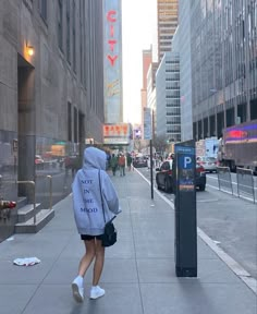 a woman walking down the street in front of tall buildings with signs on them that read city