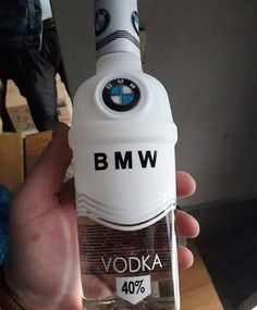 a person holding a bottle of vodka with bmw logo on the top in their hand