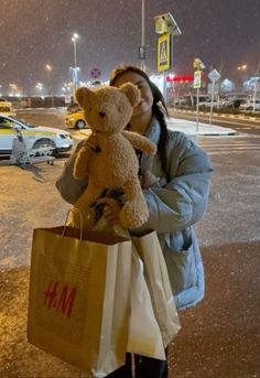 a woman is holding a teddy bear and shopping bags in the street at night time