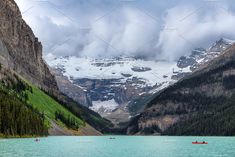 two canoes are on the water in front of snow covered mountains and evergreen trees