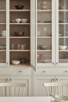 a white china cabinet with glass doors and wooden chairs