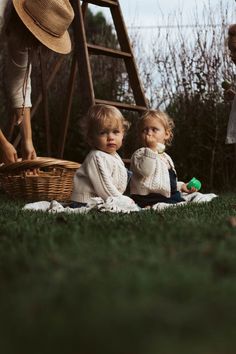 two toddlers sitting on the grass in front of a ladder