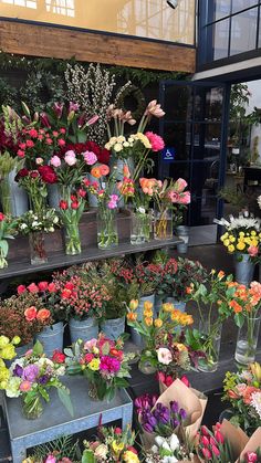 a bunch of flowers that are sitting in vases on a shelf with some plants