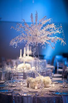 the centerpieces are decorated with white flowers, candles and frosted branches in clear vases