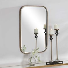 a mirror sitting on top of a wooden shelf next to two candles and a vase with flowers