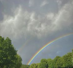 two rainbows are seen in the sky above some trees and grass on a cloudy day