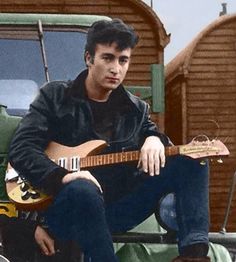 a man sitting on top of a truck holding a guitar