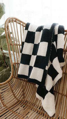 a black and white blanket sitting on top of a wicker chair next to a potted plant