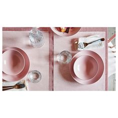 a pink place setting with dishes and utensils on the table for two people to eat