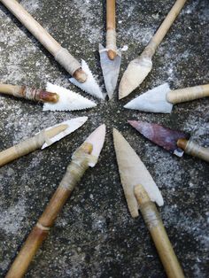 several different types of knives are arranged in a circle on the cement surface, with one knife pointed at the center