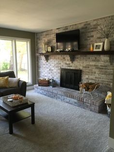 a living room filled with furniture and a fire place next to a tv mounted on a brick wall