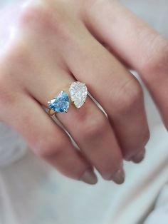 a woman's hand with two pear shaped blue and white diamond rings on it