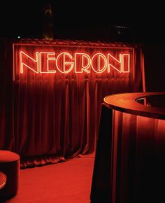 the neon sign is lit up in front of red curtained walls and stools