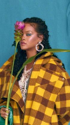 a woman holding a flower in her hand and looking at the camera while wearing a coat