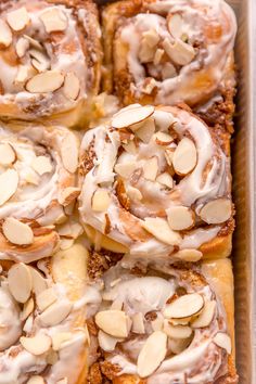 a pan filled with cinnamon rolls covered in icing and almonds