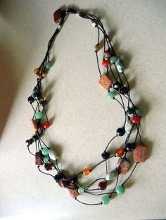 a multi stranded necklace with various beads and stones on the end, hanging from a white wall