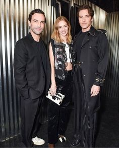 two men and a woman standing next to each other in front of a metal wall