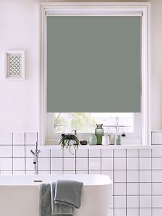 a white bath tub sitting under a window next to a green roller shade in a bathroom