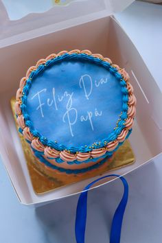 a blue frosted cake with writing on it in a pink and blue box next to a blue ribbon