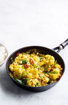 a skillet filled with food next to a bowl of rice and a spoon on the side