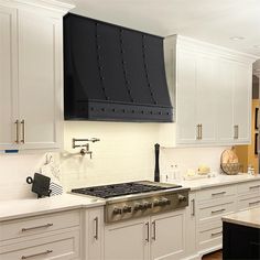 a kitchen with white cabinets and black hood over the stove, along with an island