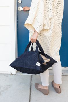 a woman carrying a black tote bag in front of a blue door