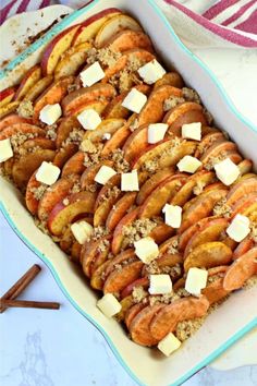 a casserole dish filled with apples, cheese and cinnamon sticks on a table