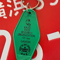 a green keychain with the words kaua field research organization and gamera on it