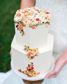 a three tiered wedding cake with colorful flowers on the top is being held by a bride