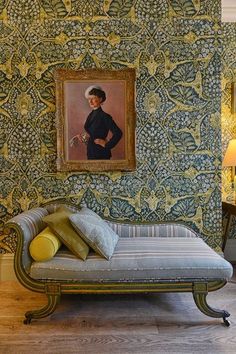 a painting hangs on the wall next to a chaise lounge in front of a portrait of a woman