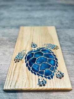 a wooden plaque with a blue sea turtle on it's side, sitting on a table