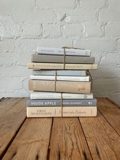 a stack of books sitting on top of a wooden table next to a white brick wall